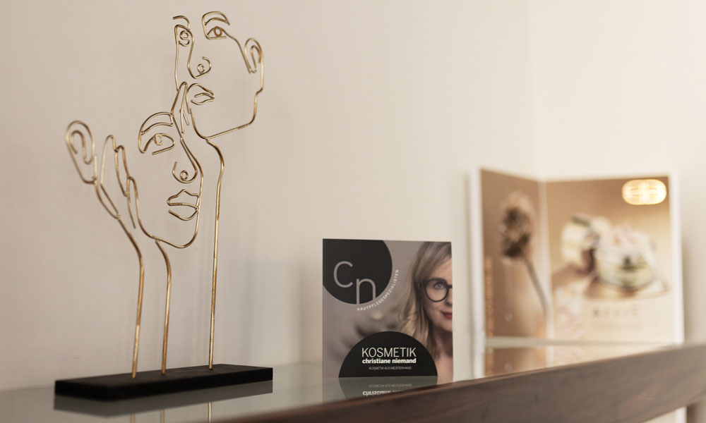 Goldene Gesichtsskulptur und Flyer von Kosmetik Christiane Niemand auf einem Regal