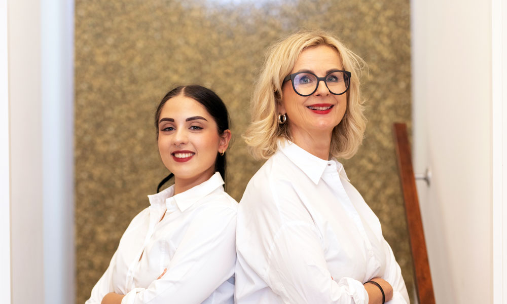 Christiane Niemand und Sophie Rösler in weißen Blusen vor der goldenen Wand